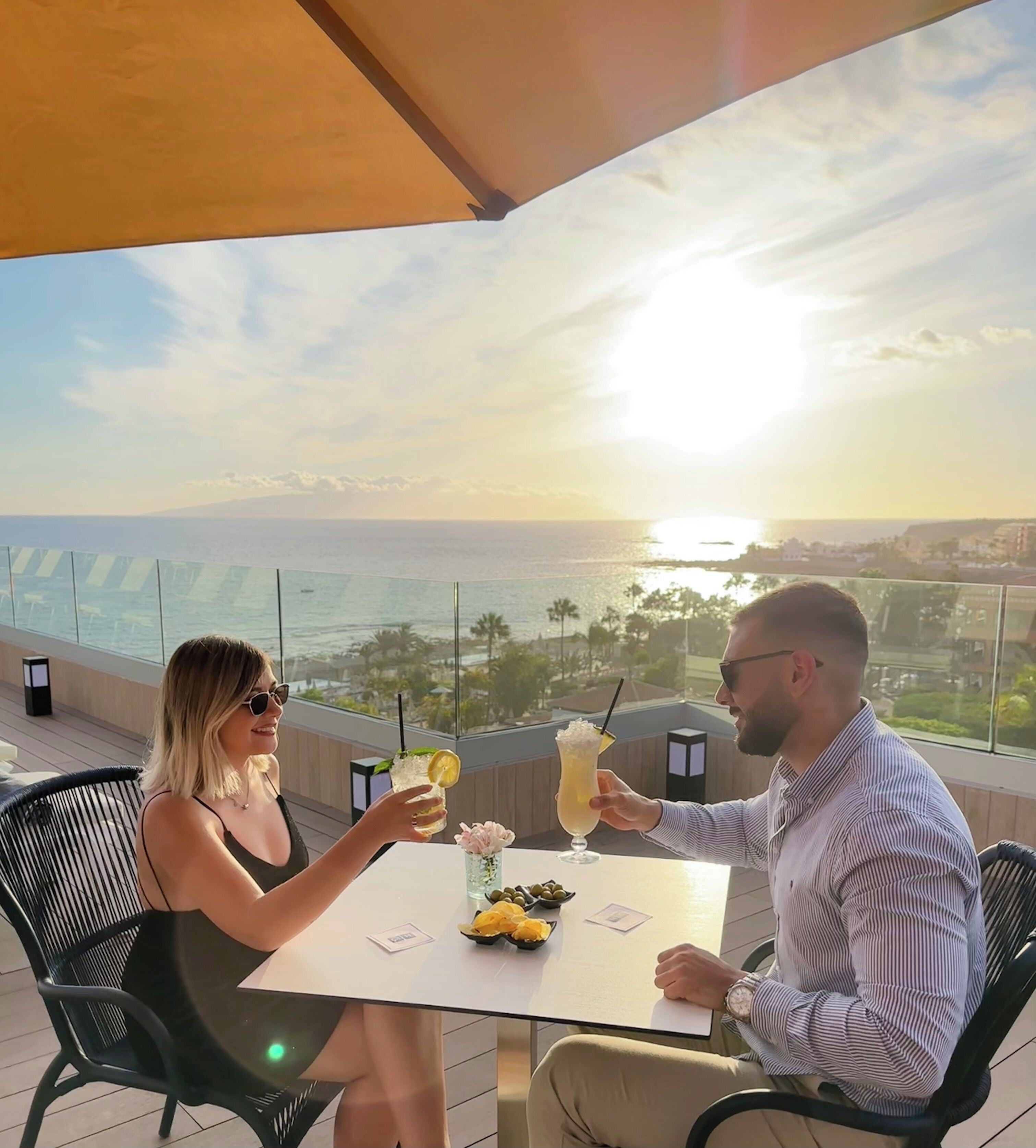A couple seated at a table with a view of the ocean and cityscape.