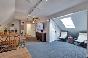 A room with a dining area, a TV, a ceiling fan, and a skylight.