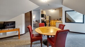 Una sala de estar moderna con una mesa de comedor de madera, sillas rojas, un televisor sobre un mueble bajo y una cocina al fondo.