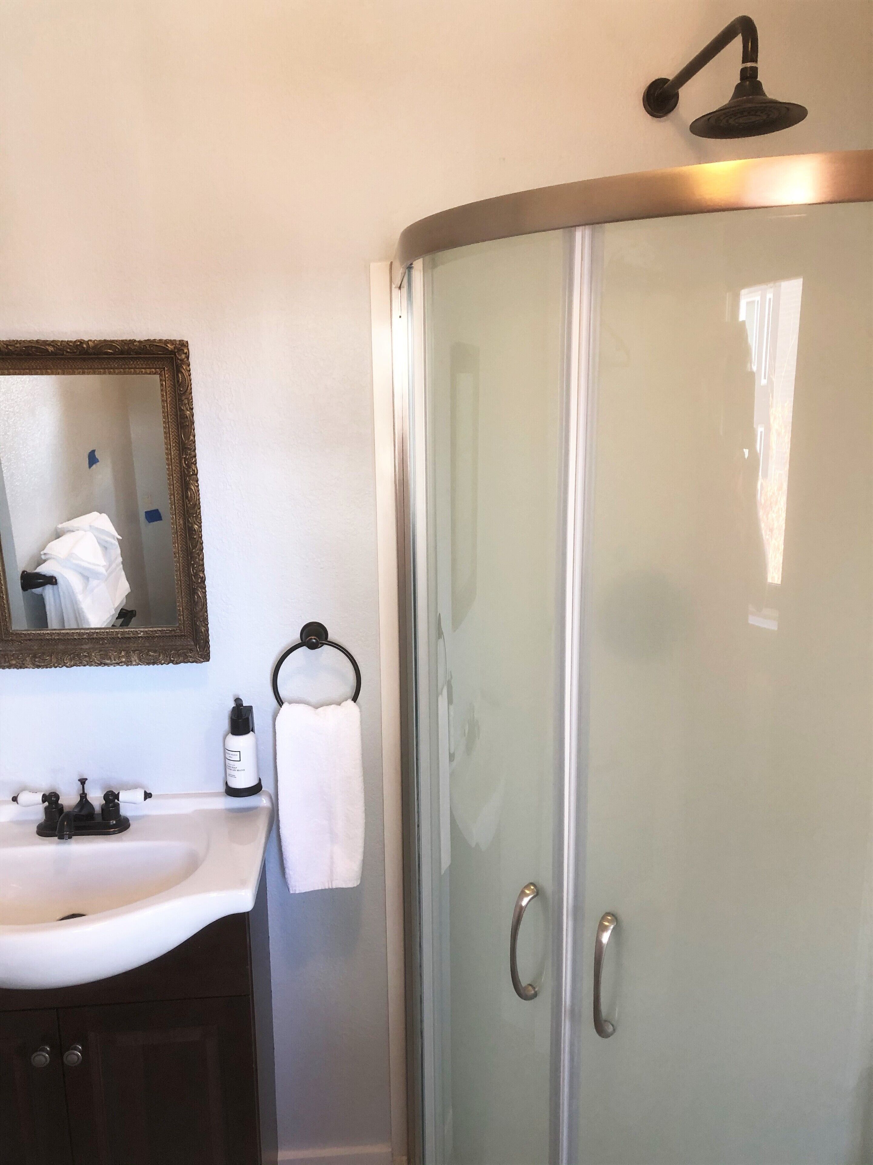 Un baño con cabina de ducha de vidrio, un lavamanos con espejo y un perchero para toallas.