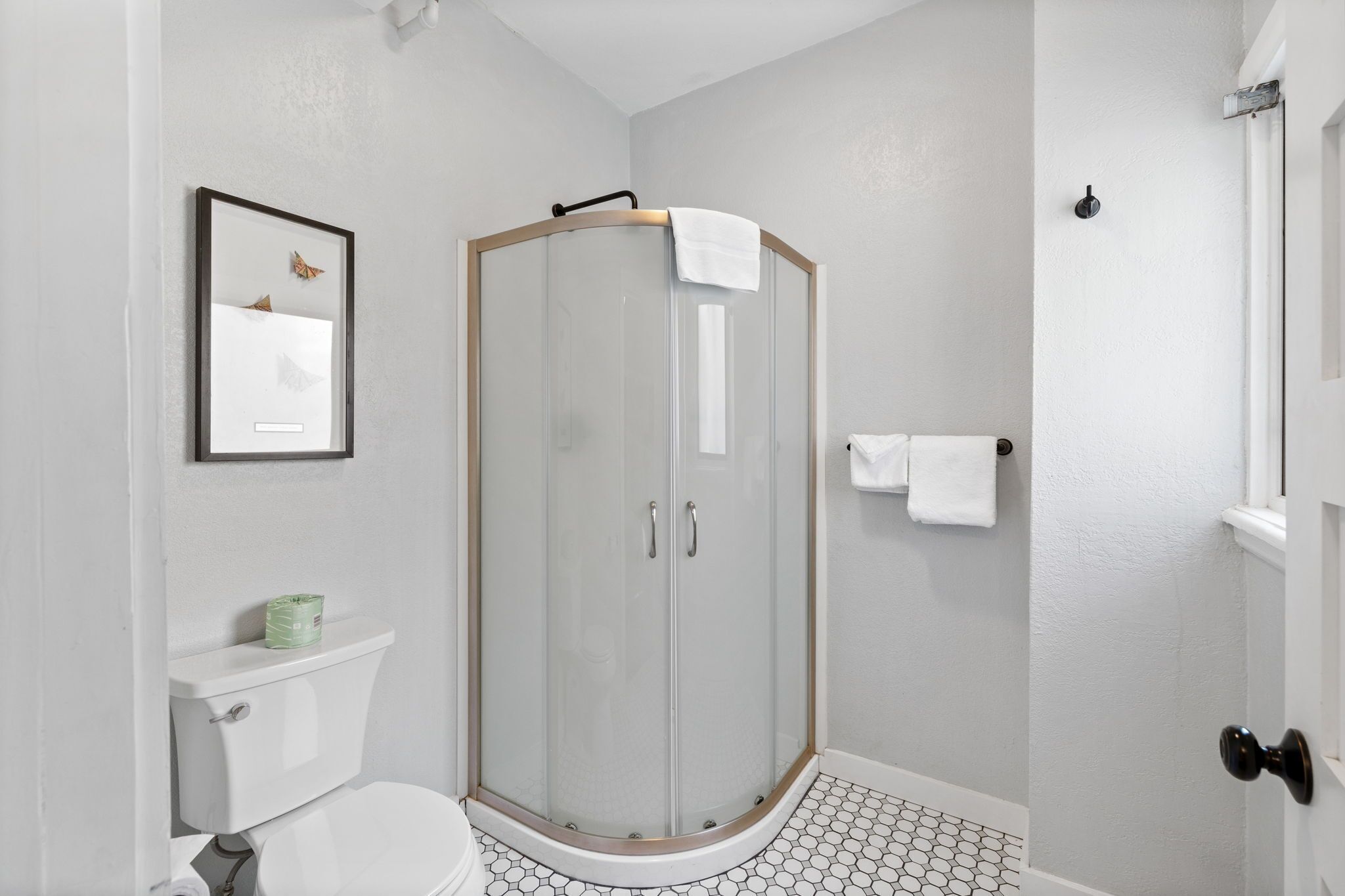 A modern bathroom with a glass-enclosed shower, a toilet, and a framed picture on the wall.