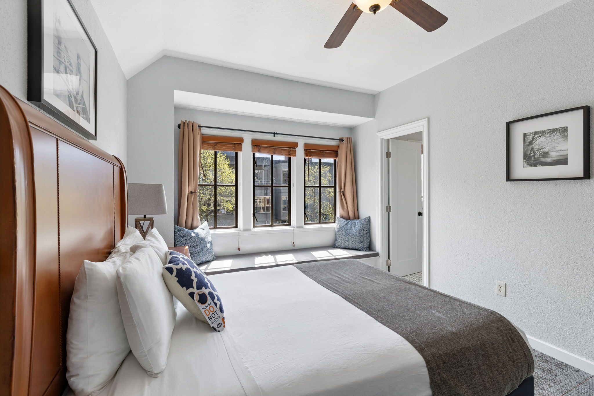 Un dormitorio con una cama grande, un asiento junto a la ventana y un ventilador de techo.