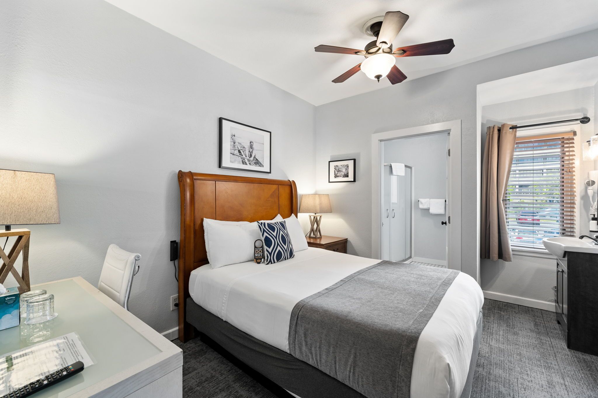 Habitación de hotel con cama, mesitas de noche, escritorio, ventilador de techo y ventana con persianas.
