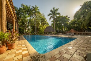 A swimming pool with tiled edges, surrounded by palm trees and a thatched-roof structure. - Mayaland Hotel & Bungalows (Chichen Itza)