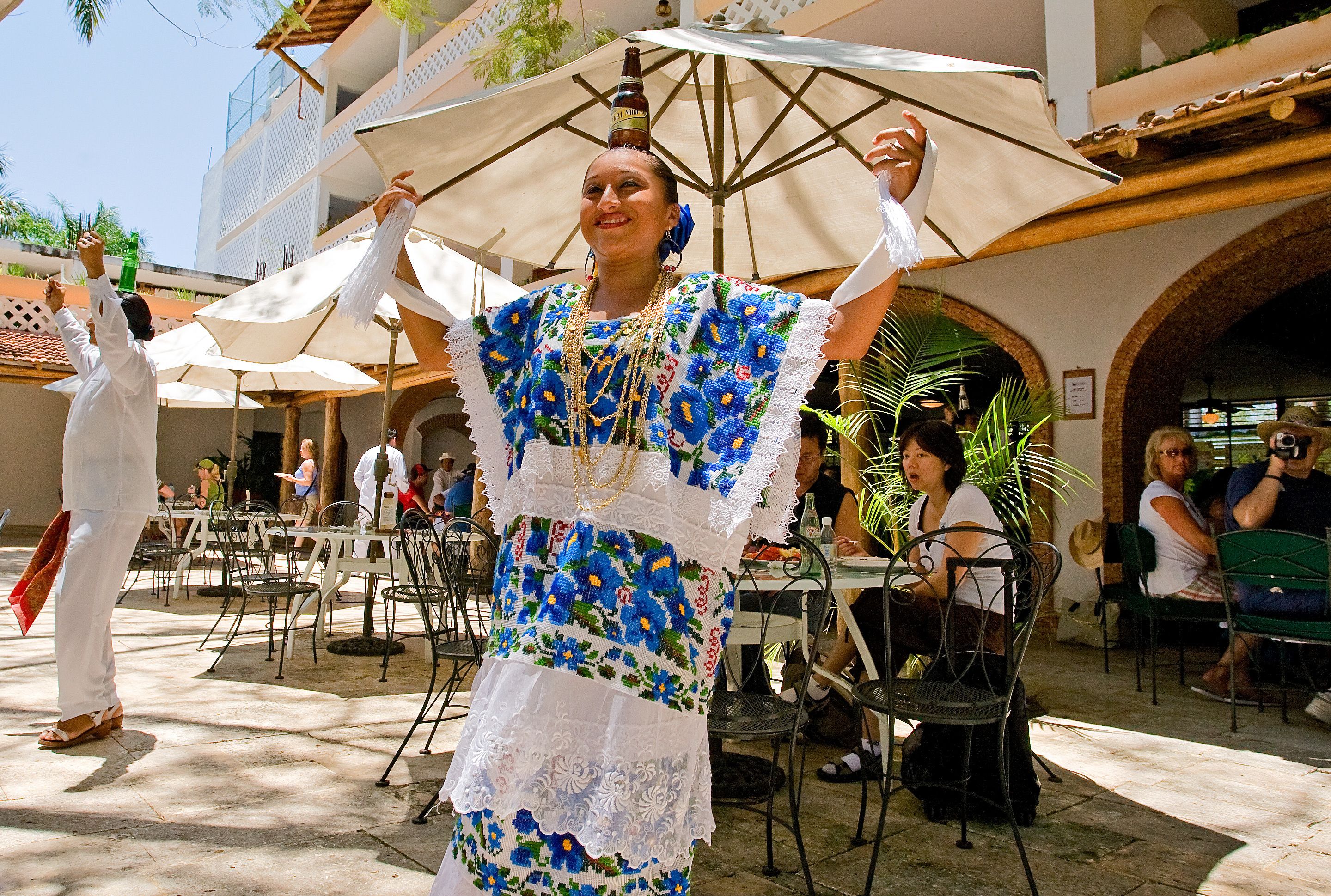 An outdoor dining area with tables and chairs, umbrellas, and people seated.