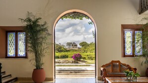A room with a large arched doorway leading to an outdoor garden, a wooden bench, and a table with a vase. - Mayaland Hotel & Bungalows (Chichen Itza)