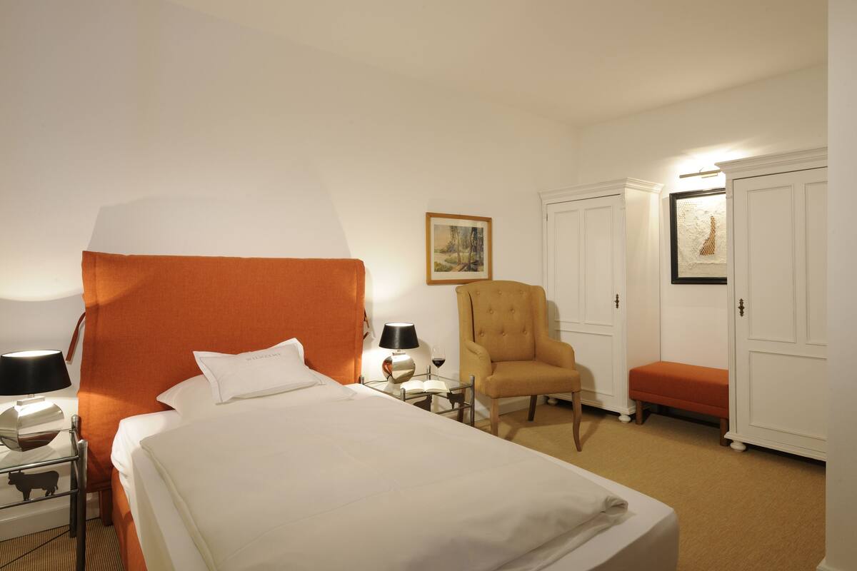 Une chambre d’hôtel avec un grand lit, une chaise, une petite table avec une lampe et un banc.