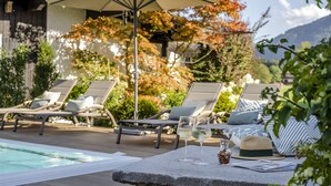 Ein Poolbereich mit Liegestühlen, einem Tisch mit Getränken und Blick auf Bäume und Berge.