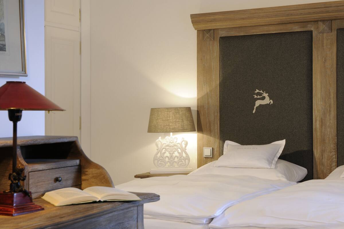 Une chambre d’hôtel avec deux lits, une table de chevet avec une lampe, une tête de lit décorative et un tableau encadré au mur.