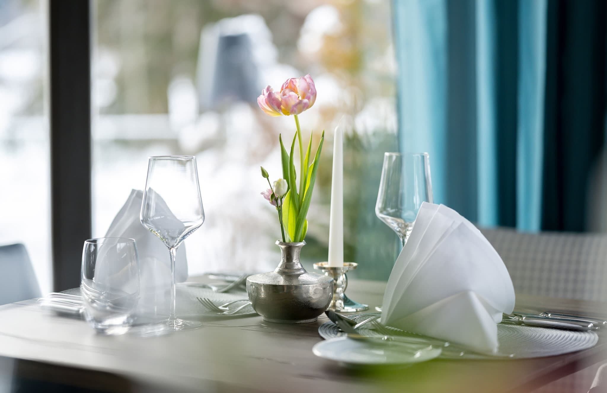 A table set for two with a vase of flowers, a candle, and clear glassware.
