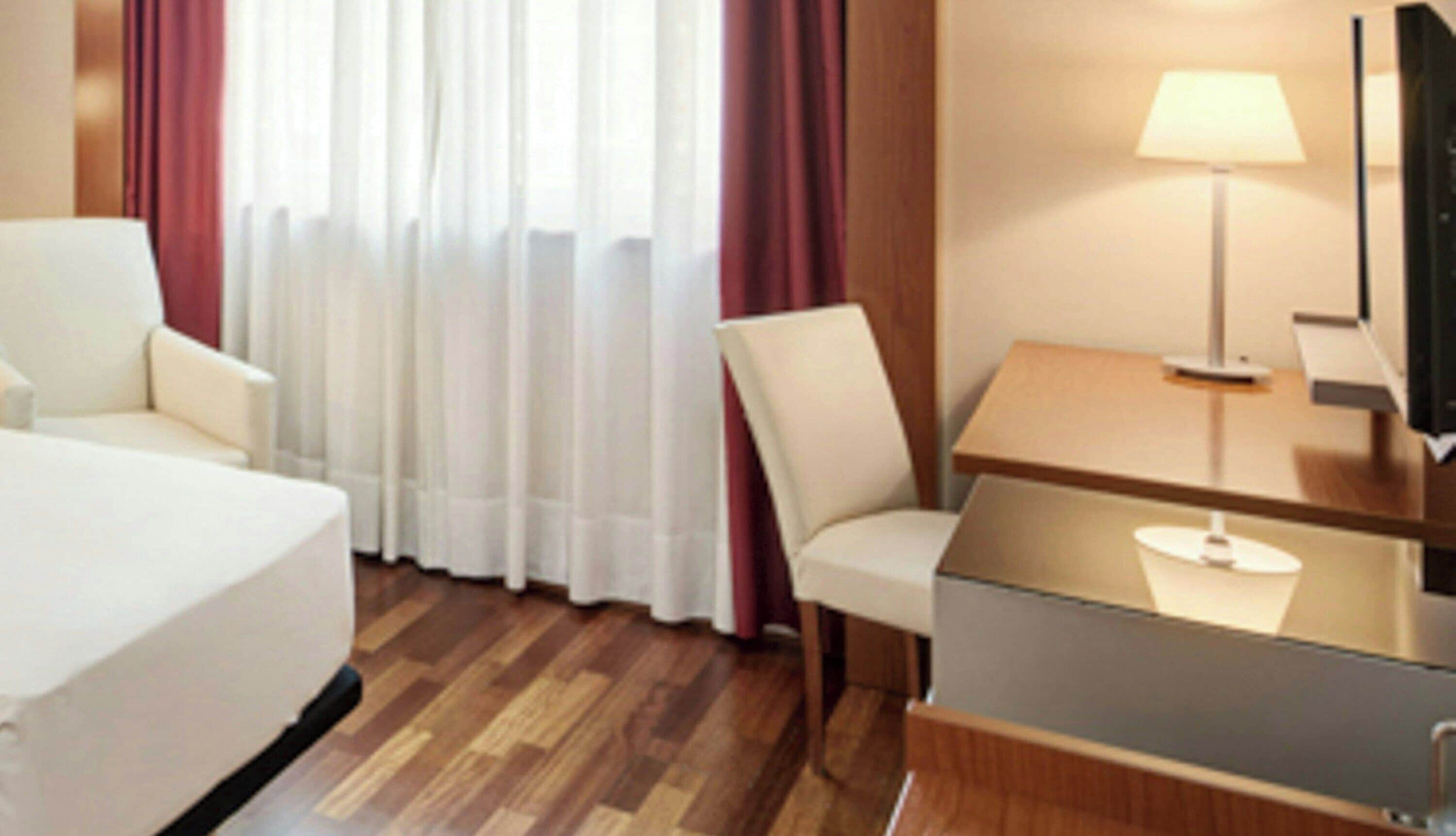 Una habitación de hotel con cama, escritorio con lámpara, silla y televisor.