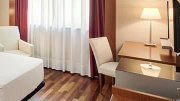 Una habitación de hotel con una cama, un escritorio con una lámpara, una silla y un televisor.