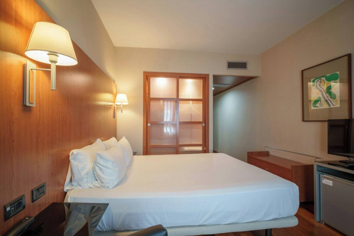 A hotel room with a bed, bedside lamps, a desk, a television, and a door leading to a staircase.