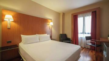 Habitación de hotel con una cama grande, dos lámparas de noche, un escritorio con silla y una ventana con cortinas.