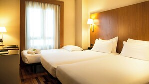A hotel room with two beds, a desk, a chair, a lamp, and a window with curtains. - Sercotel AB Arganda (Arganda del Rey)