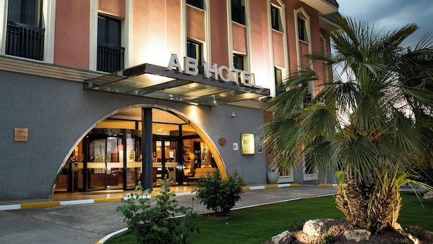 A hotel entrance with a covered entrance, a signboard, and a well-maintained lawn with a palm tree. - Sercotel AB Arganda (Arganda del Rey)