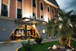 Een hotel ingang met een overdekte luifel, een bord en een verzorgd gazon met een palmboom.
