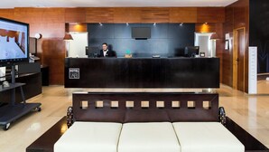 A hotel reception area with a reception desk, a television, a sofa, and a wall-mounted TV. - Sercotel AB Arganda (Arganda del Rey)