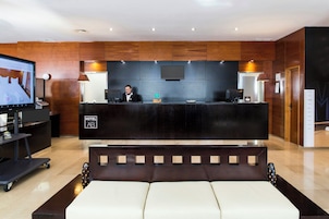 A hotel reception area with a reception desk, a television, a sofa, and a wall-mounted TV.