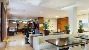 A hotel lobby with a reception desk, seating area, and a large potted plant. - Sercotel AB Arganda (Arganda del Rey)