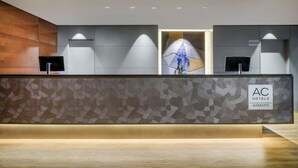 A hotel reception desk with a modern design, featuring a geometric patterned wall, a wooden accent wall, and a sign indicating the hotel name.