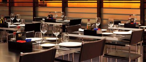 Un comedor moderno con mesas dispuestas para varios invitados, con sillas negras y un diseño limpio y contemporáneo.