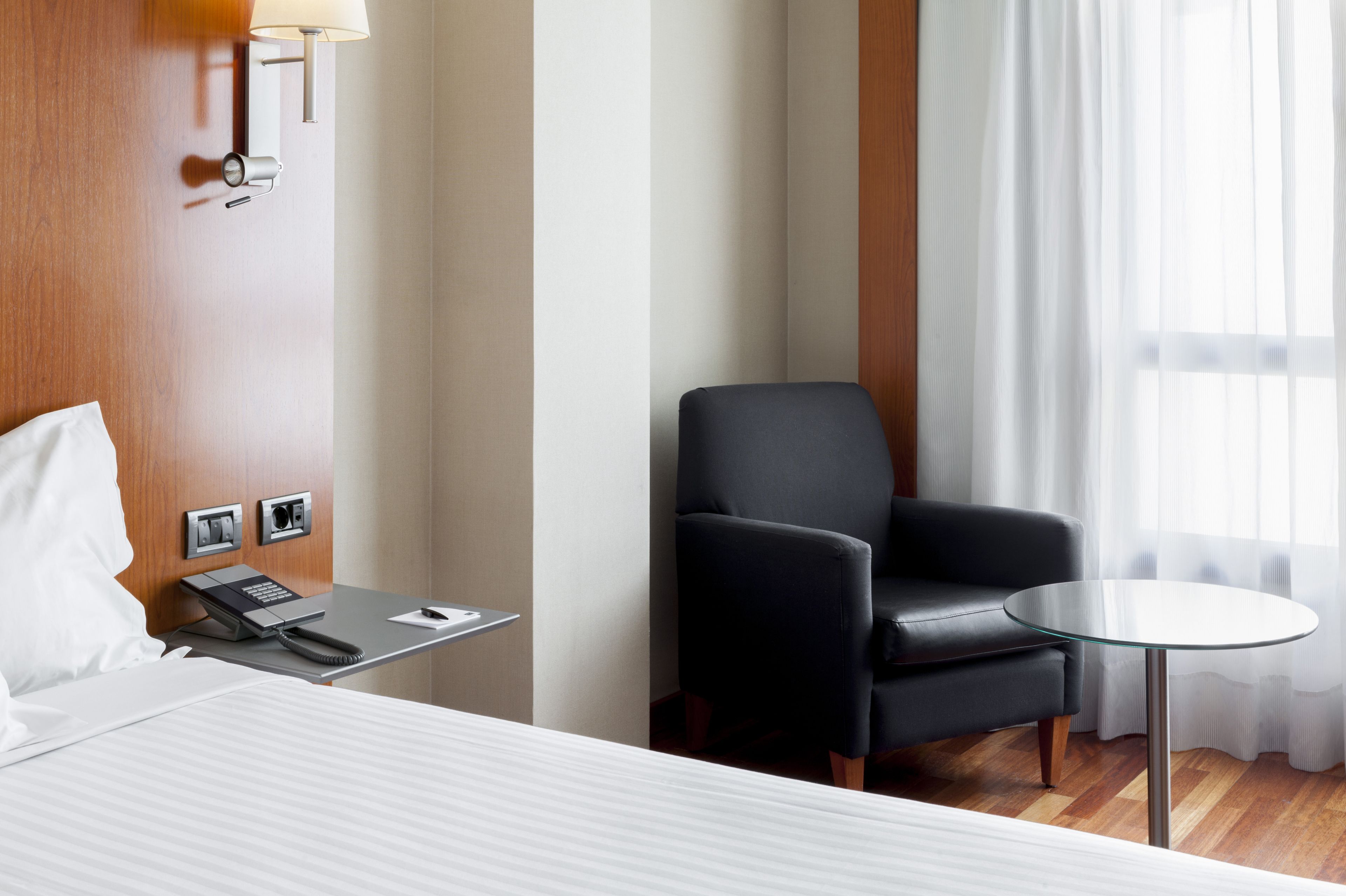 A hotel room with a bed, a desk with a telephone, a chair, and a small table.