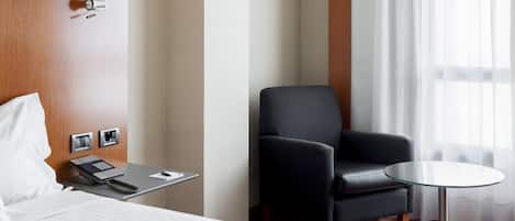 A hotel room with a bed, a desk with a telephone, a chair, and a small table.