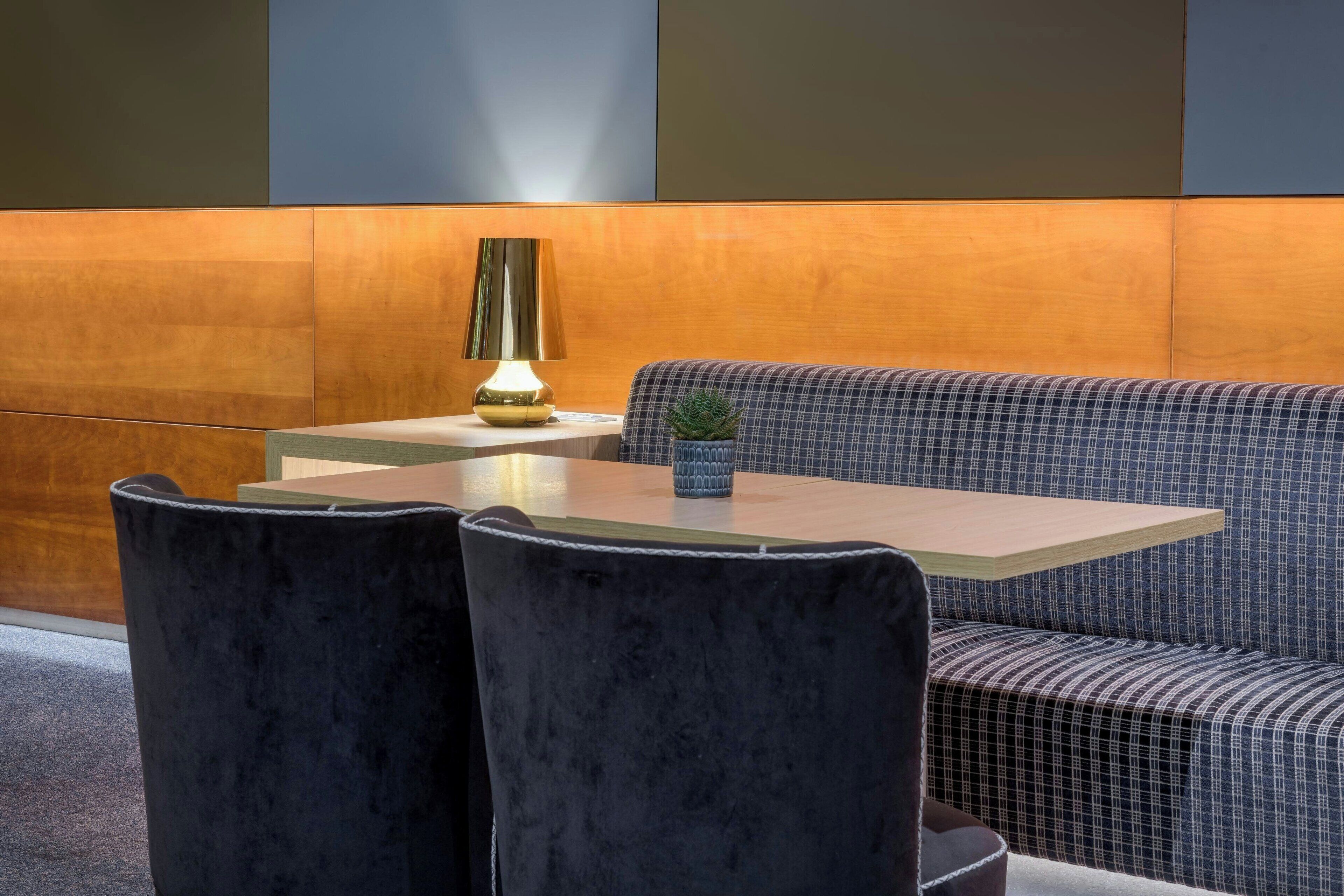 A modern dining area with a wooden table, black velvet chairs, and a checkered sofa.