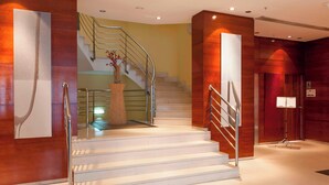 A modern hotel lobby with a staircase, a potted plant, and a reception desk.