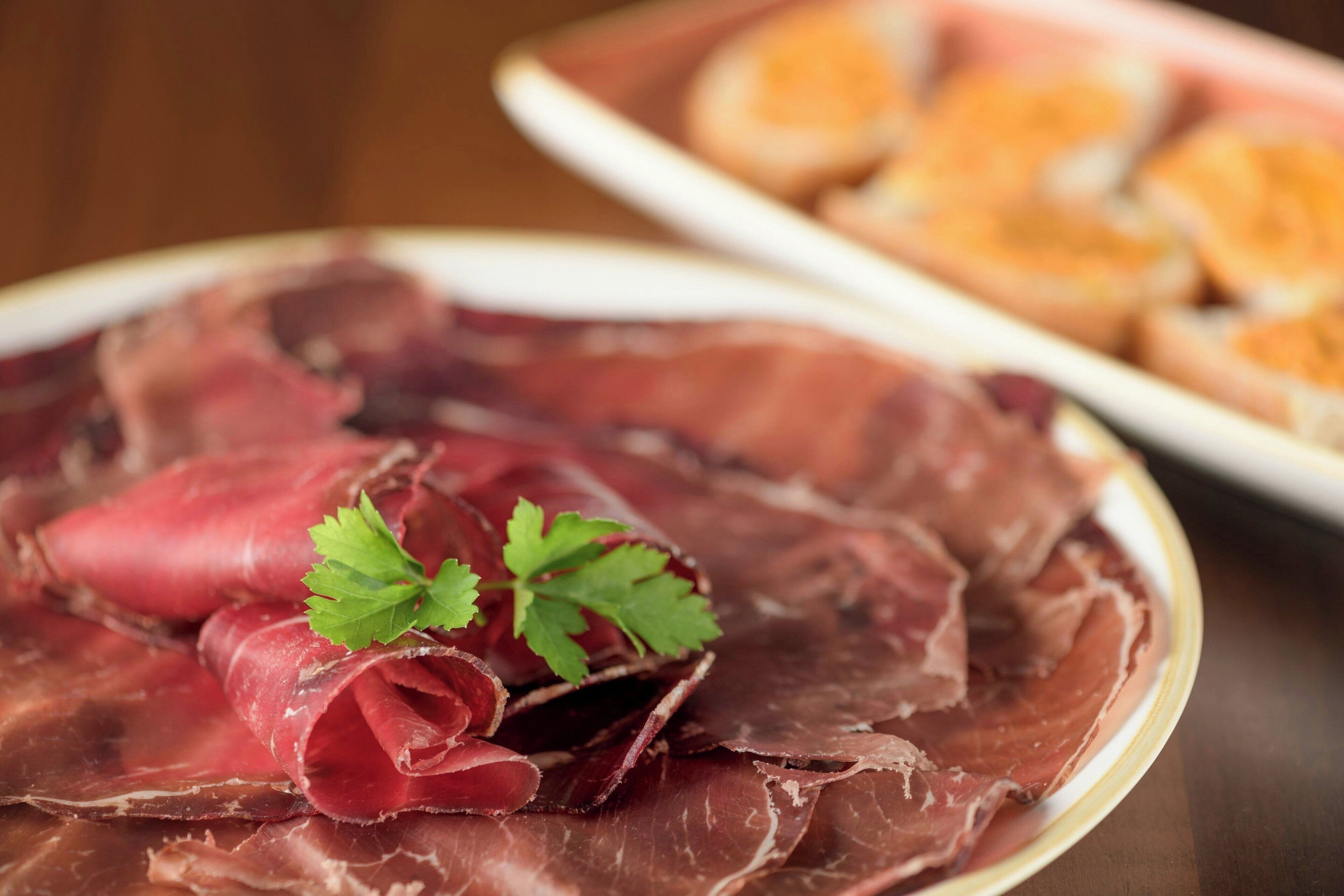 A plate of sliced cured meat with a garnish of parsley.