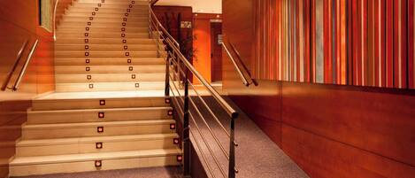Una escalera con barandilla, escalones alfombrados y una pared con paneles de madera verticales.