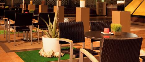 Een terras met rieten stoelen, een ronde tafel en een bloempot.