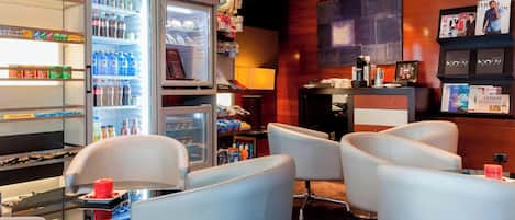 A hotel lobby with seating, a refrigerator stocked with beverages, and magazines on shelves.