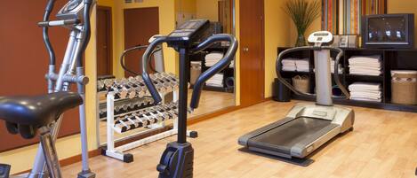A gym with exercise equipment, a treadmill, and a mirrored wall.