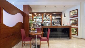 A modern bar area with a wooden counter, red chairs, and a variety of bottles on shelves.