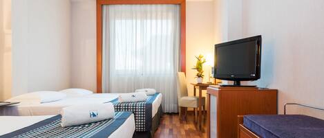 Ett hotellrum med två sängar, en tv, ett skrivbord med en lampa och en byrå i trä.