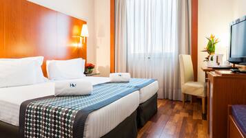 Una camera d'albergo con un letto grande, una scrivania con un computer, una sedia, una TV e una finestra con tende.