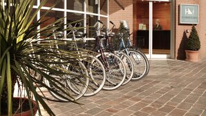 A hotel entrance with a glass facade, bicycles parked outside, and a potted plant. - EXE Toscana (Lucca)