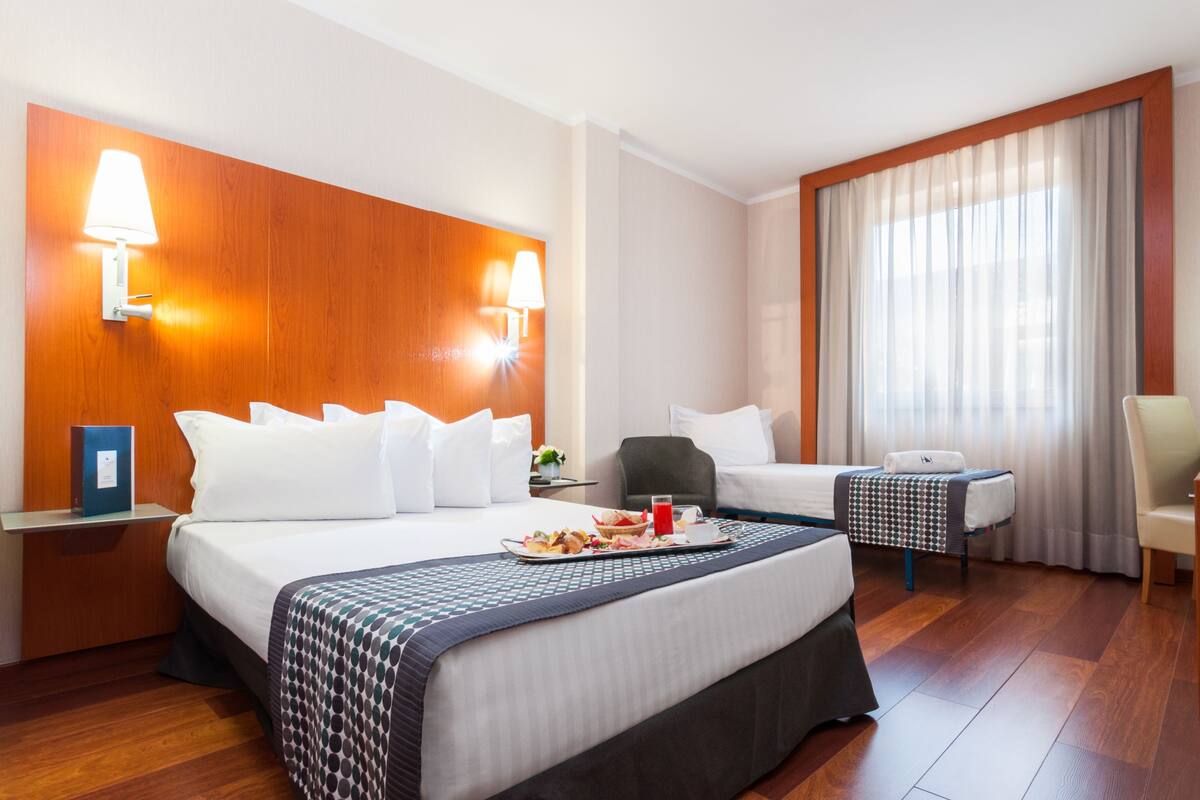 A hotel room with a large bed, a desk, a chair, and a window with curtains.