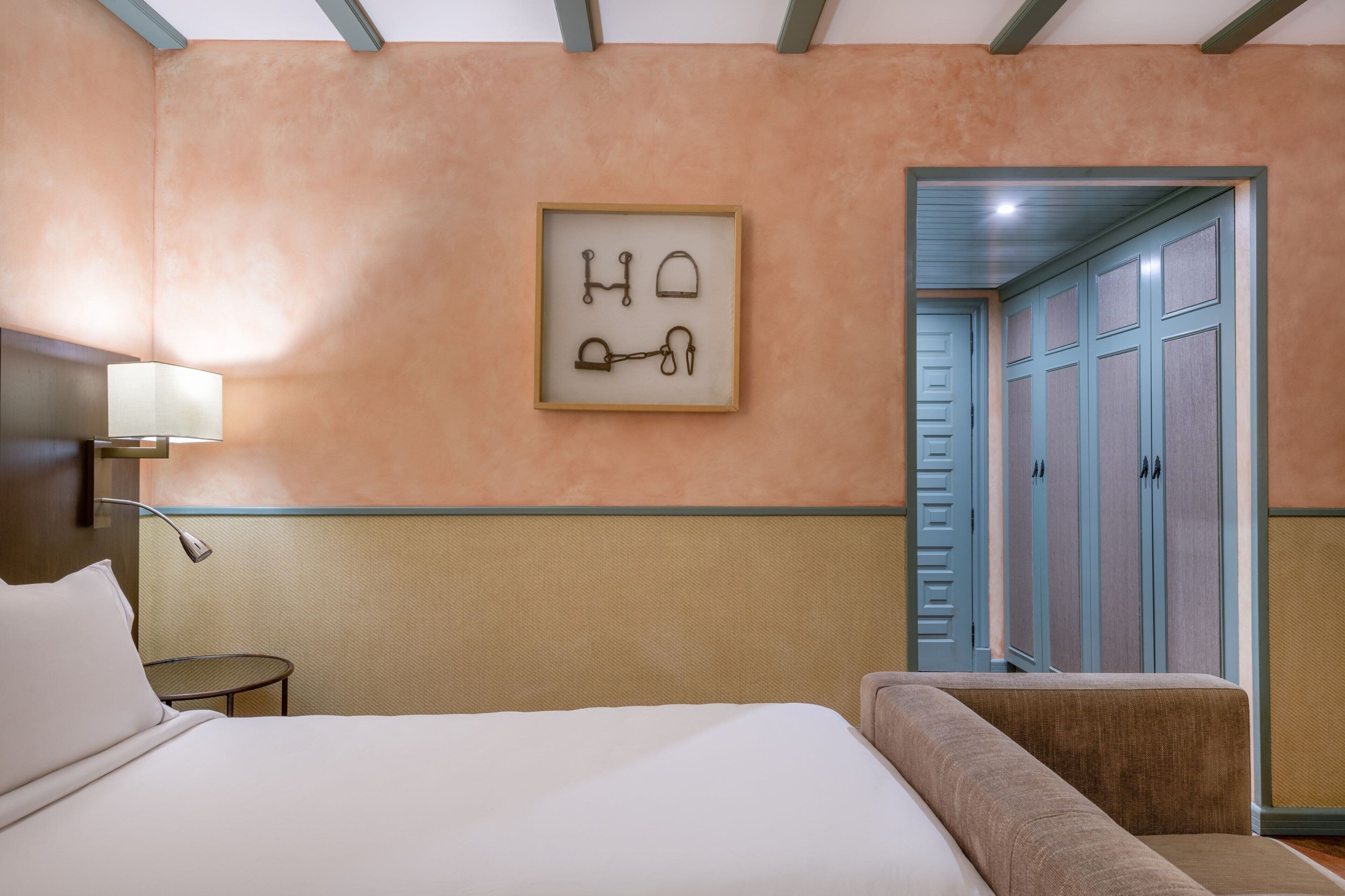 A hotel room with a bed, a small table, a chair, and a framed picture on the wall.