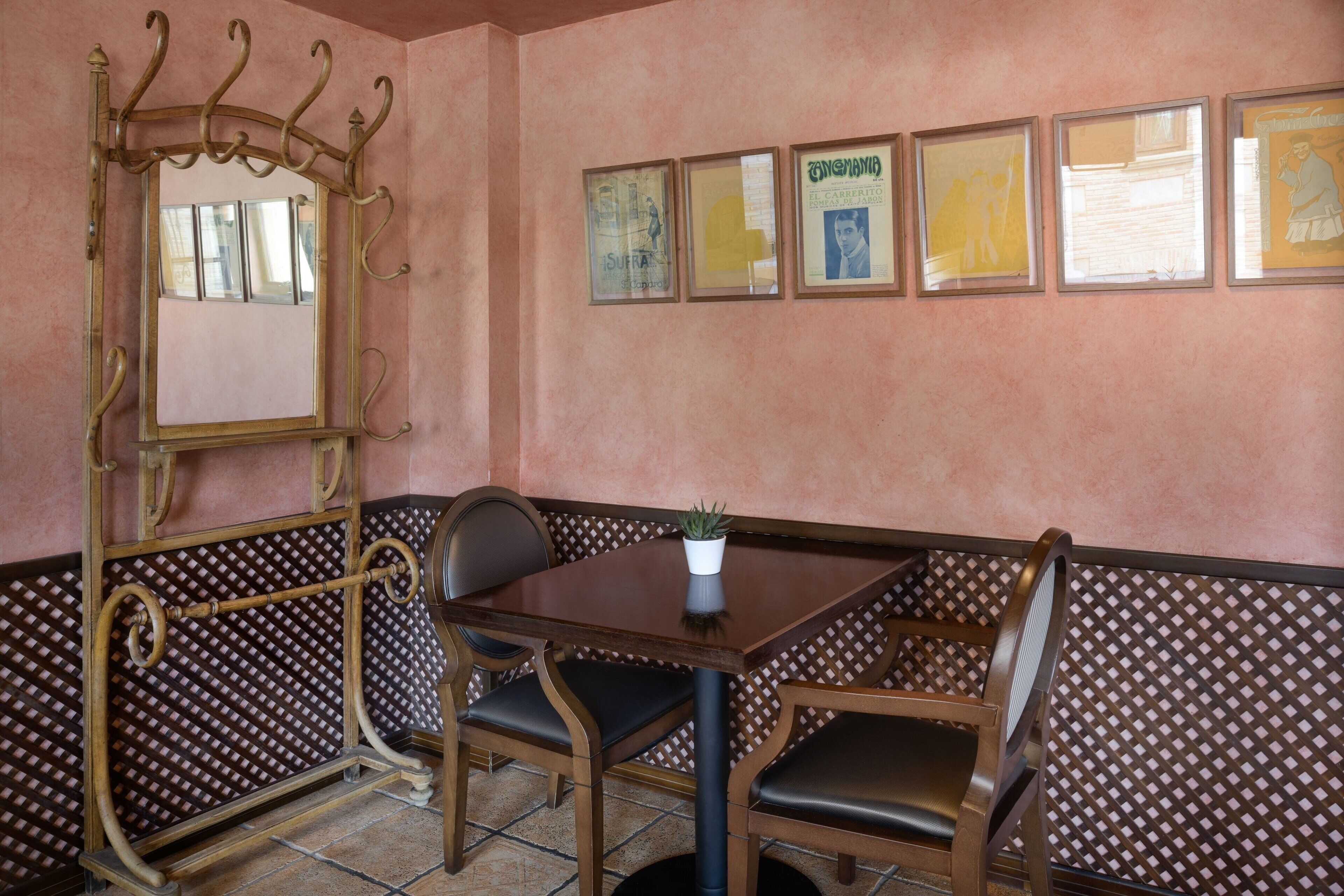 A dining area with a wooden table and chairs, a decorative mirror, and framed artwork on the wall.