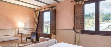 A hotel room with a bed, a sofa, a small table, a chair, and a window with curtains.