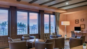 Une chambre d’hôtel dotée de grandes fenêtres, de fauteuils en cuir, d’un bureau, d’une lampe et d’un téléviseur.