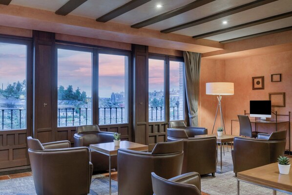Une chambre d’hôtel dotée de grandes fenêtres, de fauteuils en cuir, d’un bureau, d’une lampe et d’un téléviseur.