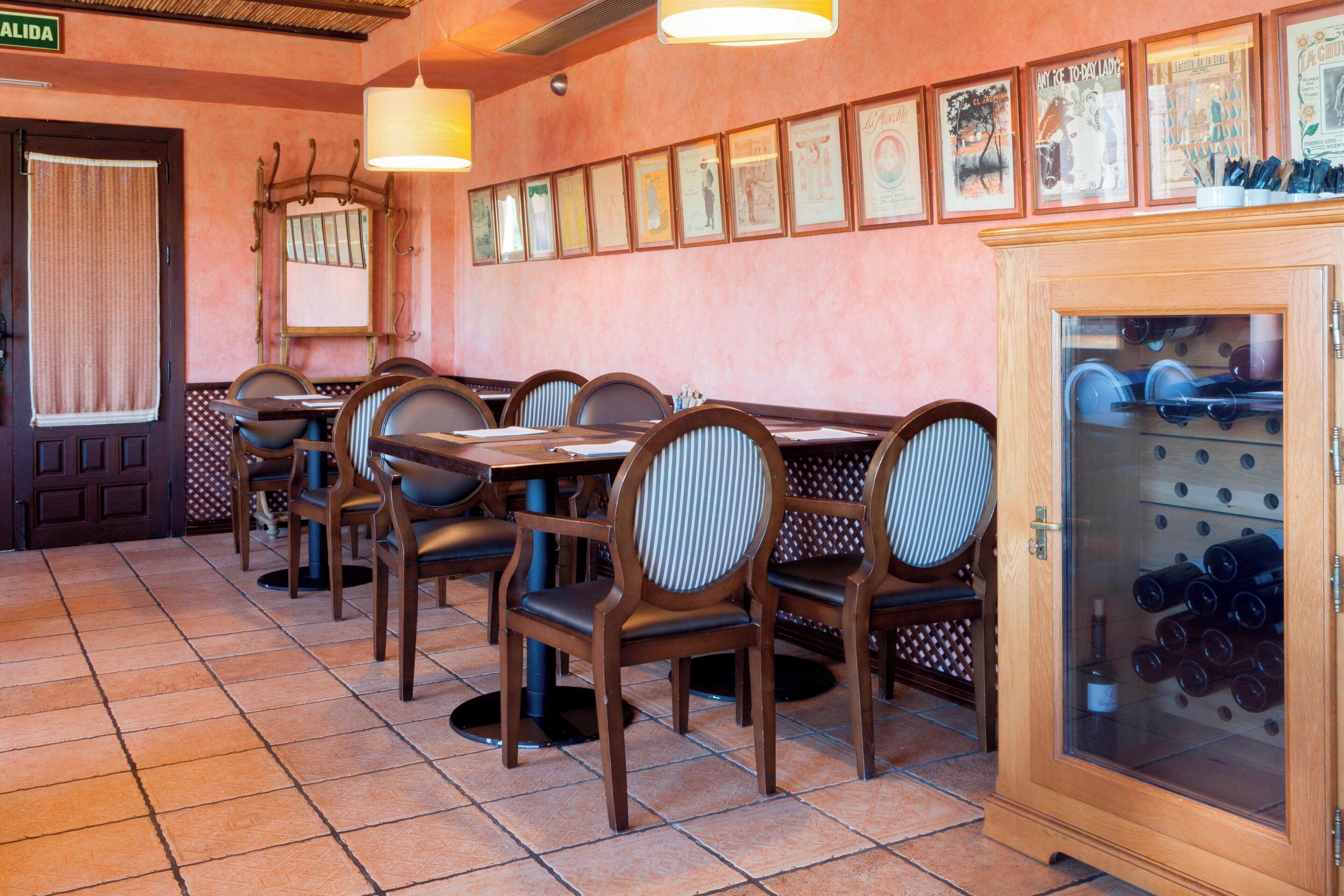 Un interior de restaurante con mesas y sillas de madera, una estantería para vinos y cuadros en la pared.