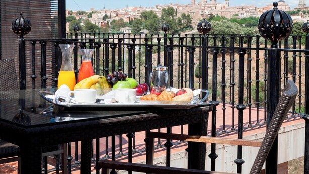 Un plateau de petit-déjeuner avec des fruits, du jus et des viennoiseries, servi sur un balcon offrant une vue sur la ville.