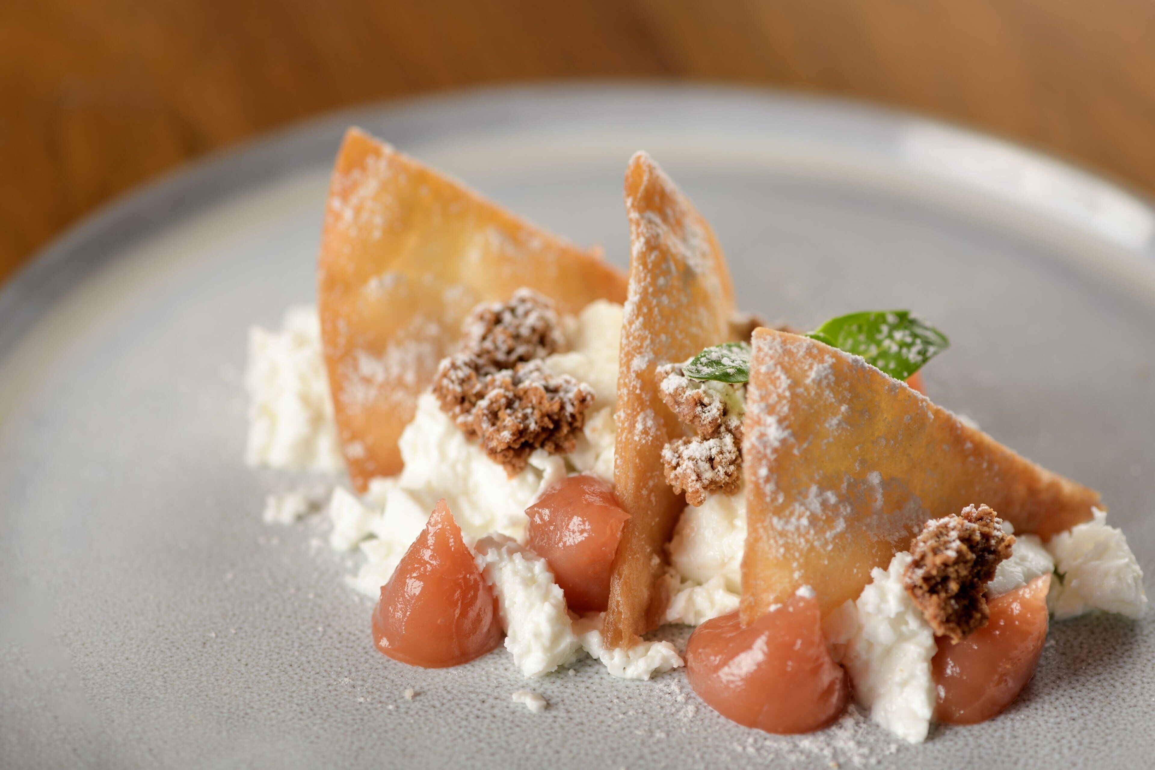A dessert with crumbled cake, cream, and a leaf garnish on a plate.