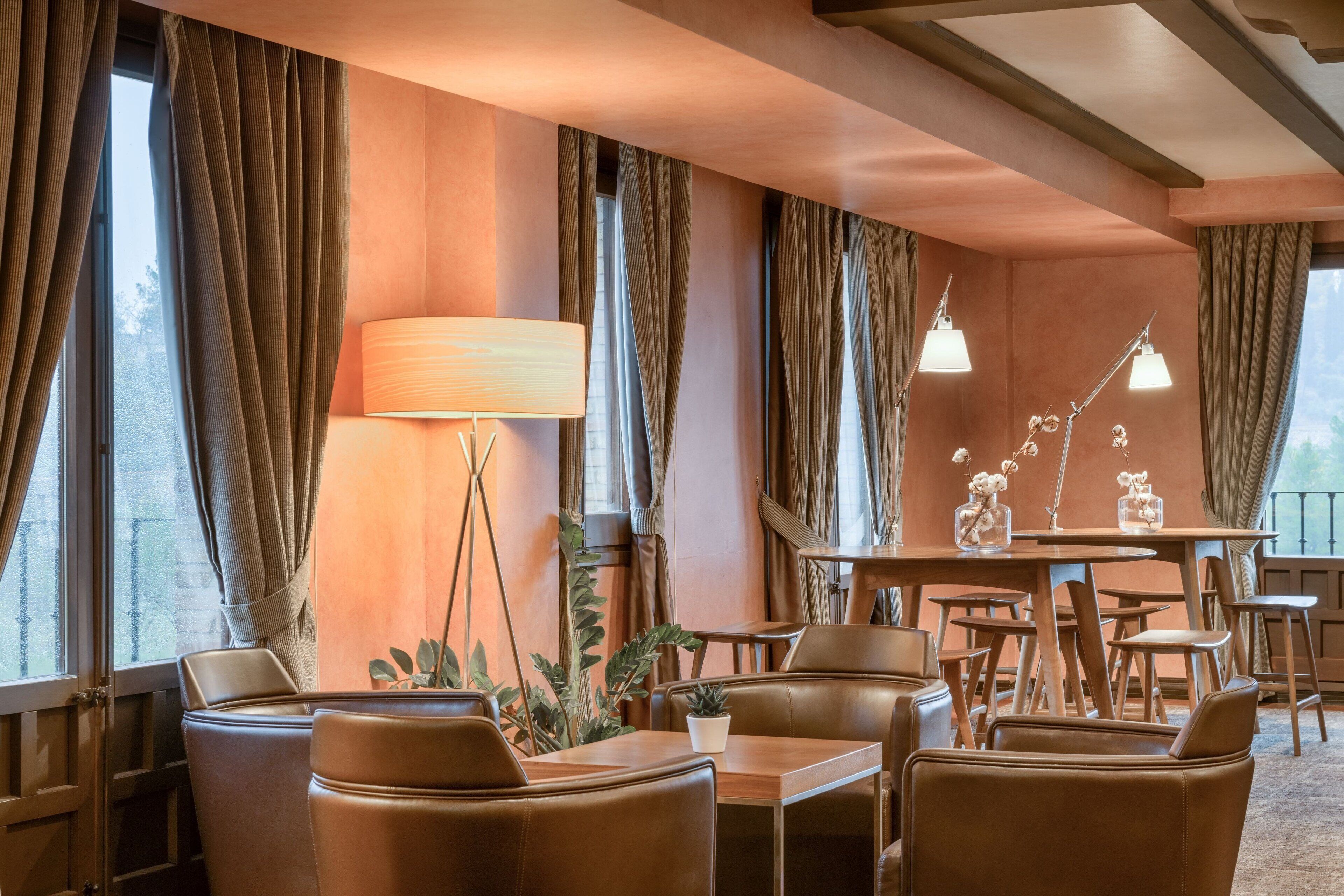 Quarto de hotel acolhedor, com poltronas de couro, uma mesa de madeira e uma janela grande com cortinas.