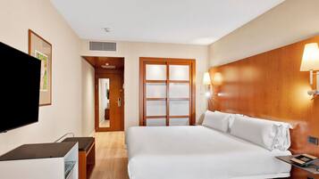 Habitación de hotel con cama, mesita de noche, televisor, armario y lámpara de pared.